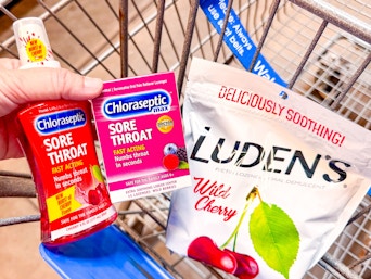 hand holding chloraseptic throat spray and lozenges with ludens drops in walmart cart