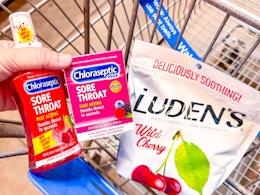 hand holding chloraseptic throat spray and lozenges with ludens drops in walmart cart