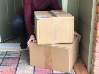 A person taking a stack of two boxes off of a front porch.
