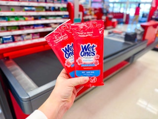 hand holding wet ones wipes in front of a checkout lane