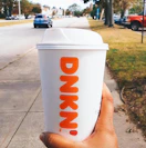 a person holding a dunkin hot coffee cup walking down the street