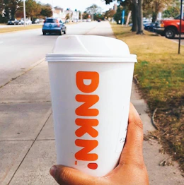 a person holding a dunkin hot coffee cup walking down the street