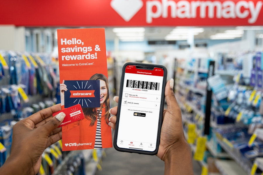 A woman holding an iphone with the CVS app, a rewards key chain card, and an extracare rewards pamphlet.