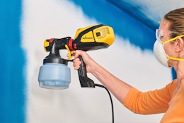 Lifestyle image of a woman spraying walls with the Wagner handheld paint sprayer