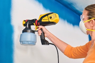 Lifestyle image of a woman spraying walls with the Wagner handheld paint sprayer