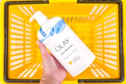 hand holding olay body wash above yellow shopping basket