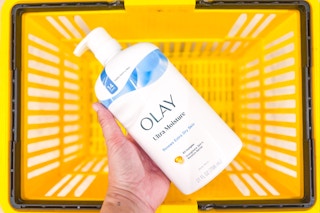 hand holding olay body wash above yellow shopping basket