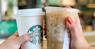 two hands holding hot and iced starbucks drinks and toasting one another