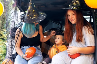 Diverse family sitting in the back of an opened car trunk with Halloween Decor