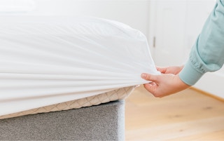 person pulling mattress protector over bed