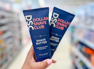 Hand holding two bottles of Dollar Shave Club Shave butters