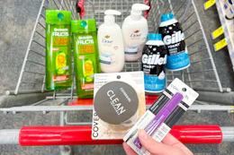 person holding covergirl setting powder and mascara over a cart with garnier shampoo, dove hand wash, and gillette foamy shave cream in it