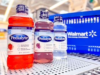 three bottles of pedialyte electrolyte solution on walmart shelf next to hand cart