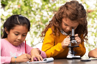 kid using microscope while other kids write in notebook