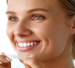 a woman using a teeth whitening strip