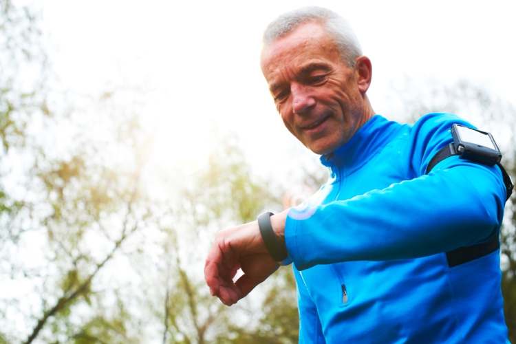 Older man in exercise clothes wearing a fitness tracker and arm band phone holder 