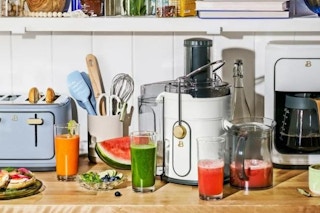 lifestyle image of a juicer on a kitchen counter surrounded by cups of juice