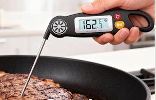 a hand holding a meat thermometer in a steak 
