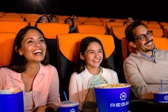 Three people with popcorn and drinks sitting inside of a theater.