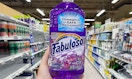 a hand holding a bottle of purple cleaner in a store aisle