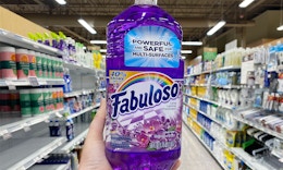 a hand holding a bottle of purple cleaner in a store aisle
