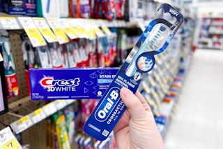 hand holding toothpaste and toothbrush in store aisle