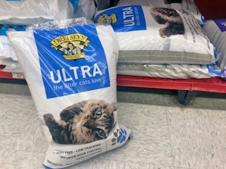 A bag of Dr. Elsey's Ultra cat litter sitting on the floor next to a shelf displaying more of the same product at Petco.