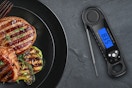 a digital meat thermometer next to a plate with steaks and vegetables