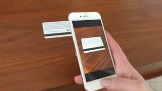 A person holding their cellphone to take a photo of the back of a gift card.