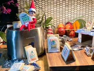 an elf on the shelf doll sitting on a toaster playing with poptarts 