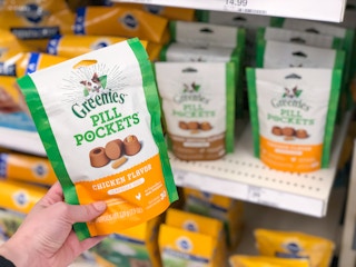 A hand holding a bag of Greenies Pill Pockets in a store aisle.