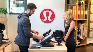 A woman standing at a Lululemon checkout counter while an employee scans her items