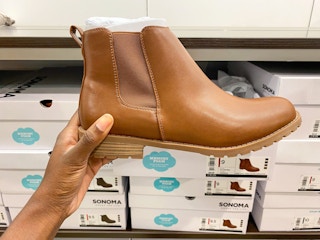 A hand holding a tan bootie in front of shoeboxes