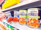 hand holding a can of progresso pitmaster soup next to others on walmart shelf