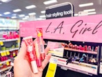 hand holding lip products in front of l.a. girl display in cvs