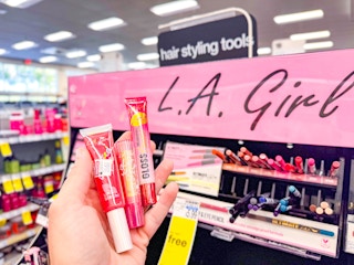 hand holding lip products in front of l.a. girl display in cvs