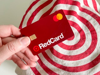 A person's hand holding a Target RedCard above a reusable Target shopping bag.
