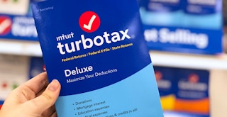 A person's hand holding up a box of TurboTax Deluxe software inside Target.