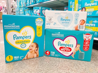 A box of Pampers Cruisers 360 fit diapers, a box of Pampers Swaddlers diapers, and a box of Pampers sensitive wipes stacked on the ...