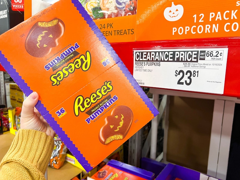 person holding a box of reeses pumpkins by a clearance sign for $23.81