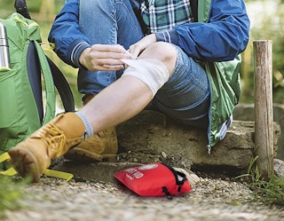 a person using a first aid kit on their knee outside