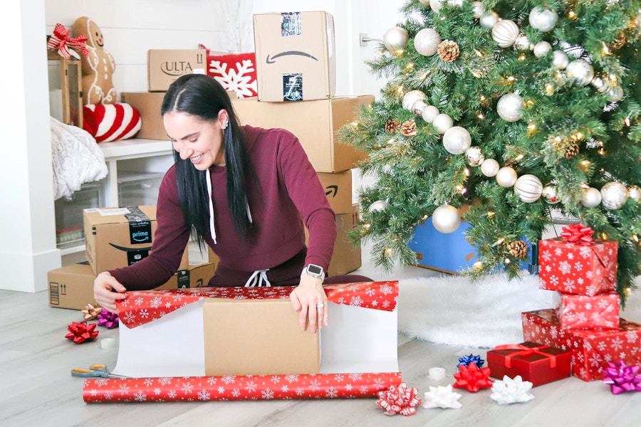 a woman wrapping gifts next to a tree with shipping boxes behind her