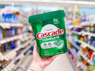 person holding a tub of cascade pods in an aisle