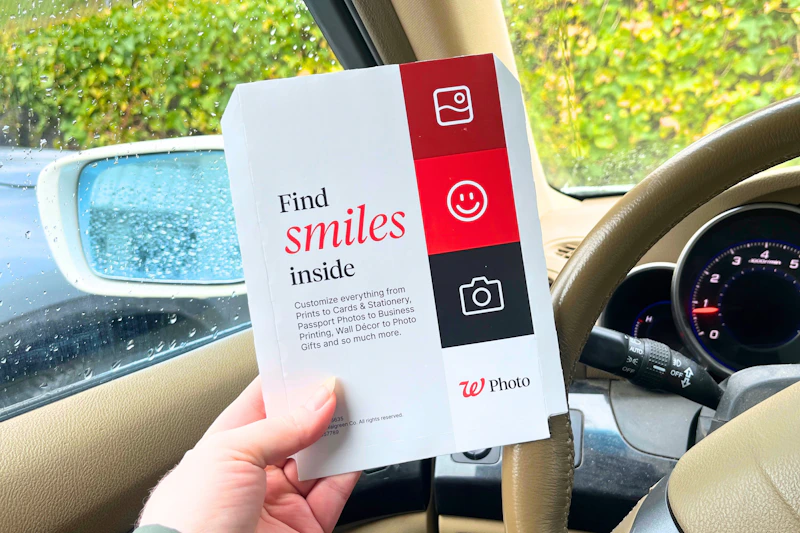 hand holding a walgreens photo packet in a car
