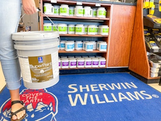 woman holding up a 5 gallon paint bucket in sherwin williams store