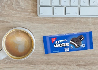a Oreo Cakester packs on a desk next to a cup of coffee