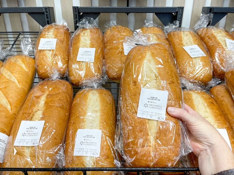 Someone picking out a loaf of bread from a shelf in the Walmart bakery section