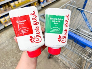 Bottles of Chick-fil-A barbeque and sweet & spicy sriracha sauce held in front of a Walmart cart