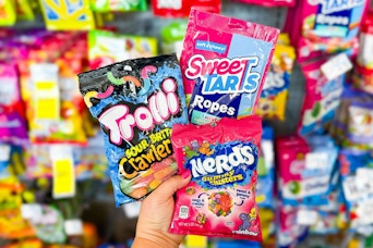 person holding bags of trolli, nerds, and sweettarts candy