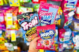 person holding bags of trolli, nerds, and sweettarts candy